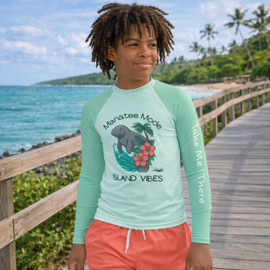 Child wearing a 'Manatee Mode Island Vibes' shirt by the ocean