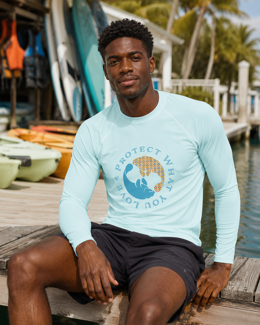 A man sitting on a wooden dock wearing a light blue long-sleeve rash guard with a blue and gold graphic on the chest that reads 'PROTECT WHAT YOU LOVE'.