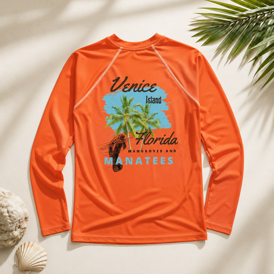 An orange long-sleeve rash guard shirt laid flat on a light beige background with decorative seashells and palm leaves. The shirt features a graphic print on the front with a blue sky, green palm tree, a stingray, and text reading 'Venice Island Florida Mangroves and Manatees'.