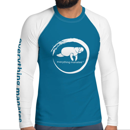 A man wearing a blue rash guard with a white logo depicting a manatee on the front. The shirt has long sleeves and is designed for water activities, providing UPF 50+ protection.