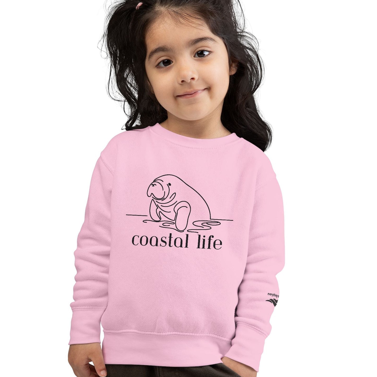 Child wearing a pink sweatshirt with 'coastal life' and a seal design on a white background