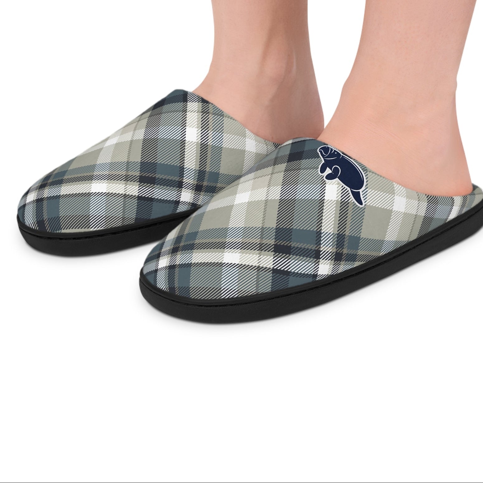 A pair of plaid slip-on slippers worn on a person's feet, shown against a plain white background. The slippers feature a muted plaid pattern in gray, navy, beige, and white, with a small navy blue beaver logo on the outer side.