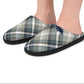 A pair of plaid slip-on slippers worn on a person's feet, shown against a plain white background. The slippers feature a muted plaid pattern in gray, navy, beige, and white, with a small navy blue beaver logo on the outer side.