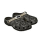 A pair of Croc-style clogs with a black and gray palm leaf pattern, featuring a beige strap with a black logo.