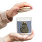 Person holding a candle with a design on the label against a white background