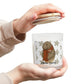 Person holding a small glass jar with a bear design and 'Classic Charm' text on a white background