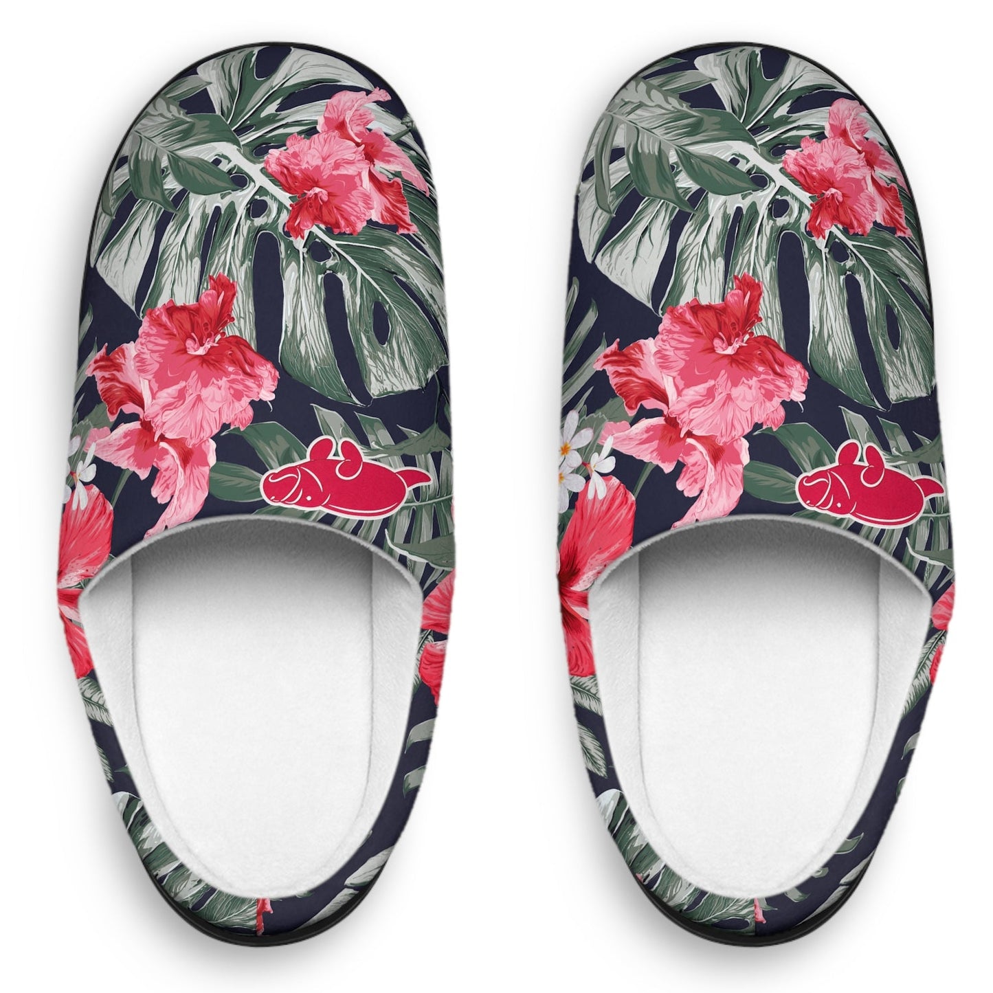 A pair of slip-on mule slippers featuring a tropical floral print with pink hibiscus flowers, green palm leaves, and red hibiscus blossoms on a dark navy background, shown from a top-down view on a white background.