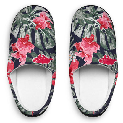 A pair of slip-on mule slippers featuring a tropical floral print with pink hibiscus flowers, green palm leaves, and red hibiscus blossoms on a dark navy background, shown from a top-down view on a white background.