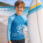 Child in blue rash guard with ocean design holding a surfboard on a beach