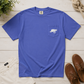 A royal blue short-sleeve pocket t-shirt with a white graphic of a kneeling dog on the chest pocket, styled in a flat lay with white pants, brown boat shoes, rope, and a plant on a white wood plank background.