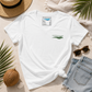 A white short-sleeve V-neck T-shirt laid flat on a light beige surface with a knot at the bottom hem. The shirt has a small green chest graphic reading 'everything financial' with a leaf motif.