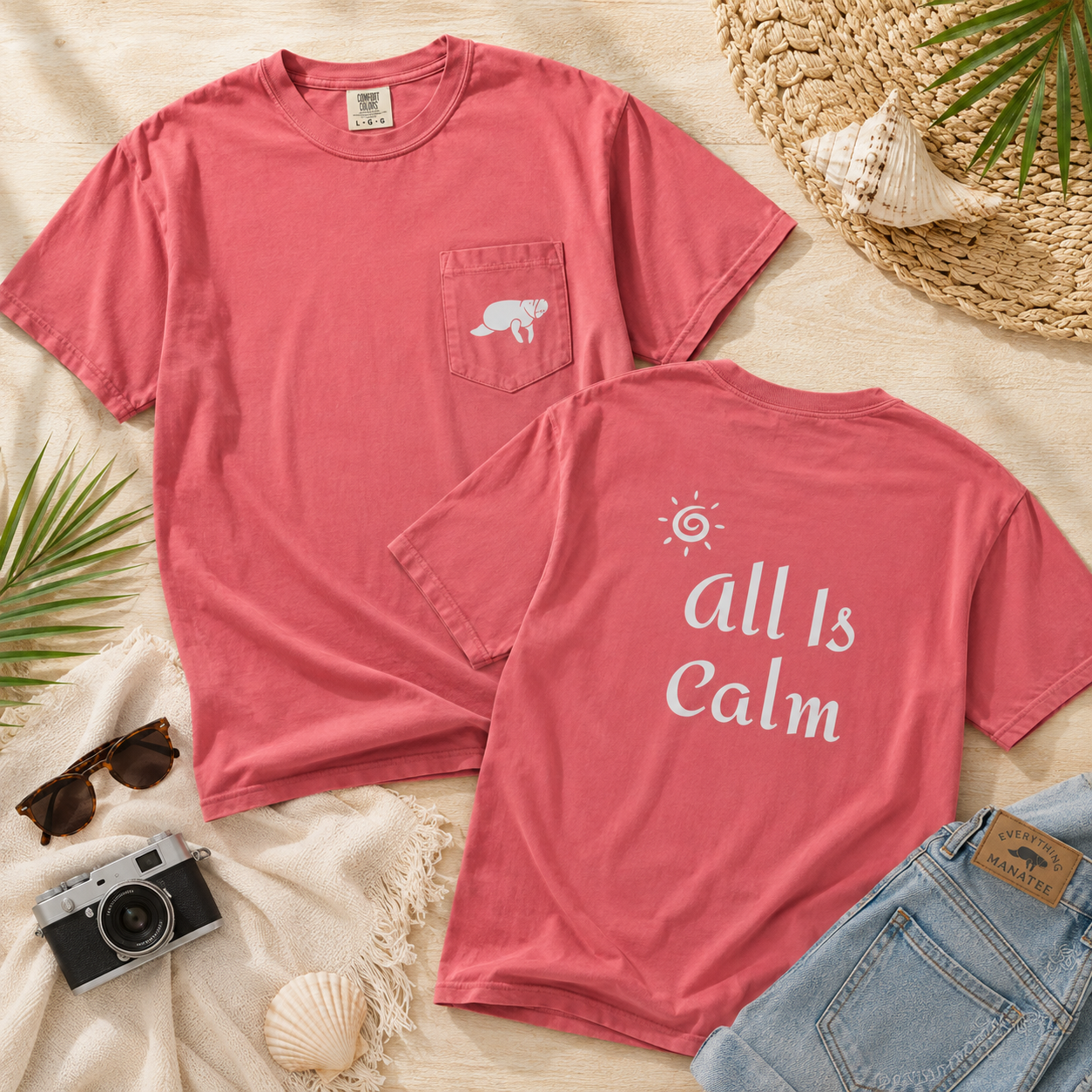 Two coral pink t-shirts arranged in a flat lay on a beige fabric background. The front shirt has a small white bear graphic on the chest pocket, and the back shirt has the words 'all Is Calm' in white script with a small sun graphic above it.