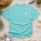 A mint green short-sleeve t-shirt with a white wave graphic and 'Everything Matters' text on the left chest, styled in a flat lay with a straw hat, seashells, starfish, and palm leaves on a white wood background.
