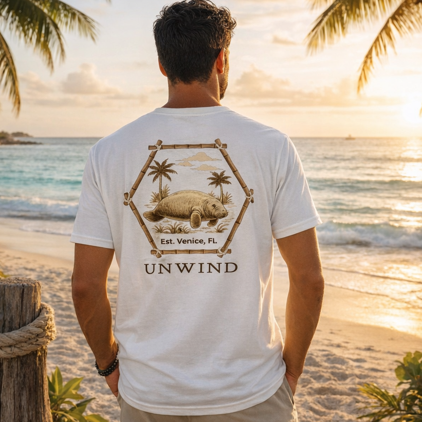 Man wearing a 'UNWIND' t-shirt with a beach design on a tropical beach at sunset.