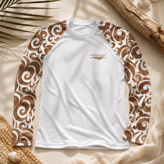 A long-sleeve raglan shirt laid flat on a beige fabric surface with decorative palm leaves, driftwood, and woven straw. The shirt is white with brown and white scroll-patterned sleeves and a small chest logo reading 'everything natural™'.