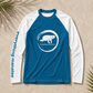 A long-sleeve raglan shirt laid flat on a textured beige surface with palm leaves in the corners. The shirt is blue on the torso and sleeves, with white sleeves and a white circular turtle logo on the chest.