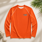 An orange long-sleeve rash guard with white contrast stitching and a small 'everything marine' logo on the left chest, displayed in a flat-lay arrangement with seashells and palm leaves on a light beige background.