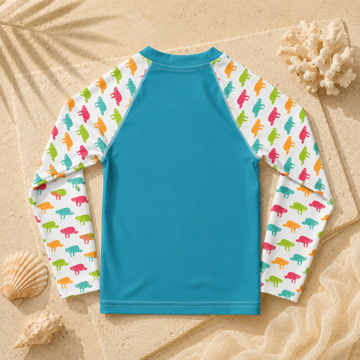 A long-sleeve rash guard swimsuit laid flat on a sandy background with seashells and netting. The back of the shirt is solid turquoise blue, and the sleeves have a white background patterned with small colorful dinosaur silhouettes in pink, orange, green, and blue.