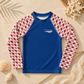 A long-sleeve kids' rash guard laid flat on a sandy surface with seashells and beach props. The shirt has a solid royal blue torso and sleeves with a red-and-white crab pattern, plus a small white 'everything marine' wave logo on the chest.