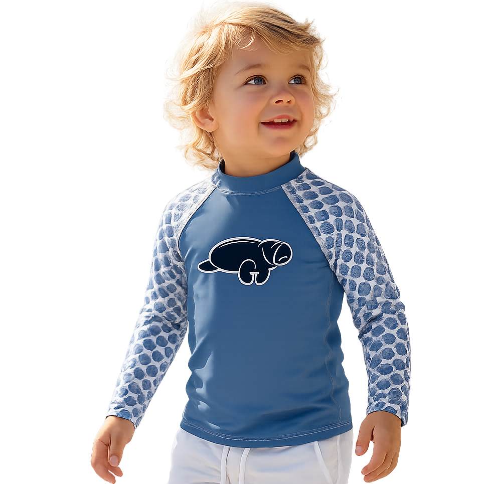 A toddler standing in shallow water wearing a blue long-sleeve rash guard with patterned sleeves and white shorts against a white background.