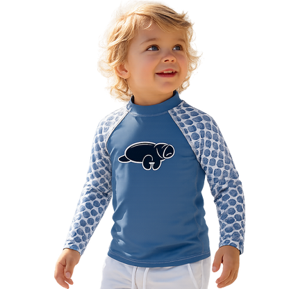 A toddler standing in shallow water wearing a blue long-sleeve rash guard with patterned sleeves and white shorts against a white background.