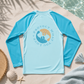 Blue long-sleeve shirt with a graphic design on a sandy surface near water
