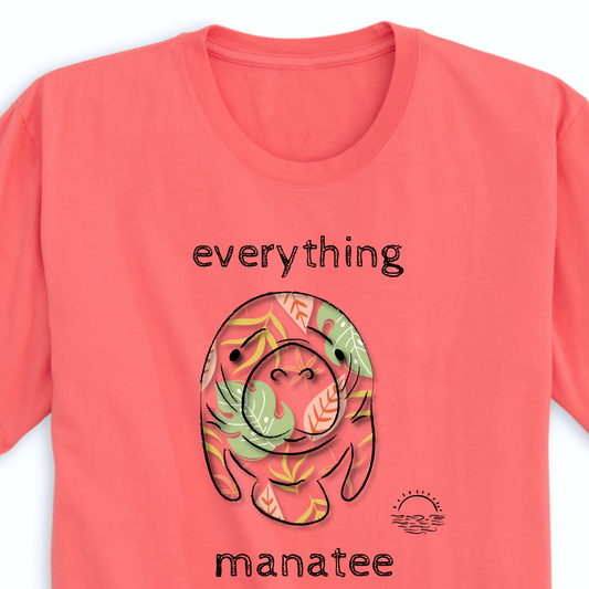 A close-up view of the front print design of the Coral Palms Manatee T-Shirt, depicting a colorful and playful manatee with tropical flowers and plants around it.