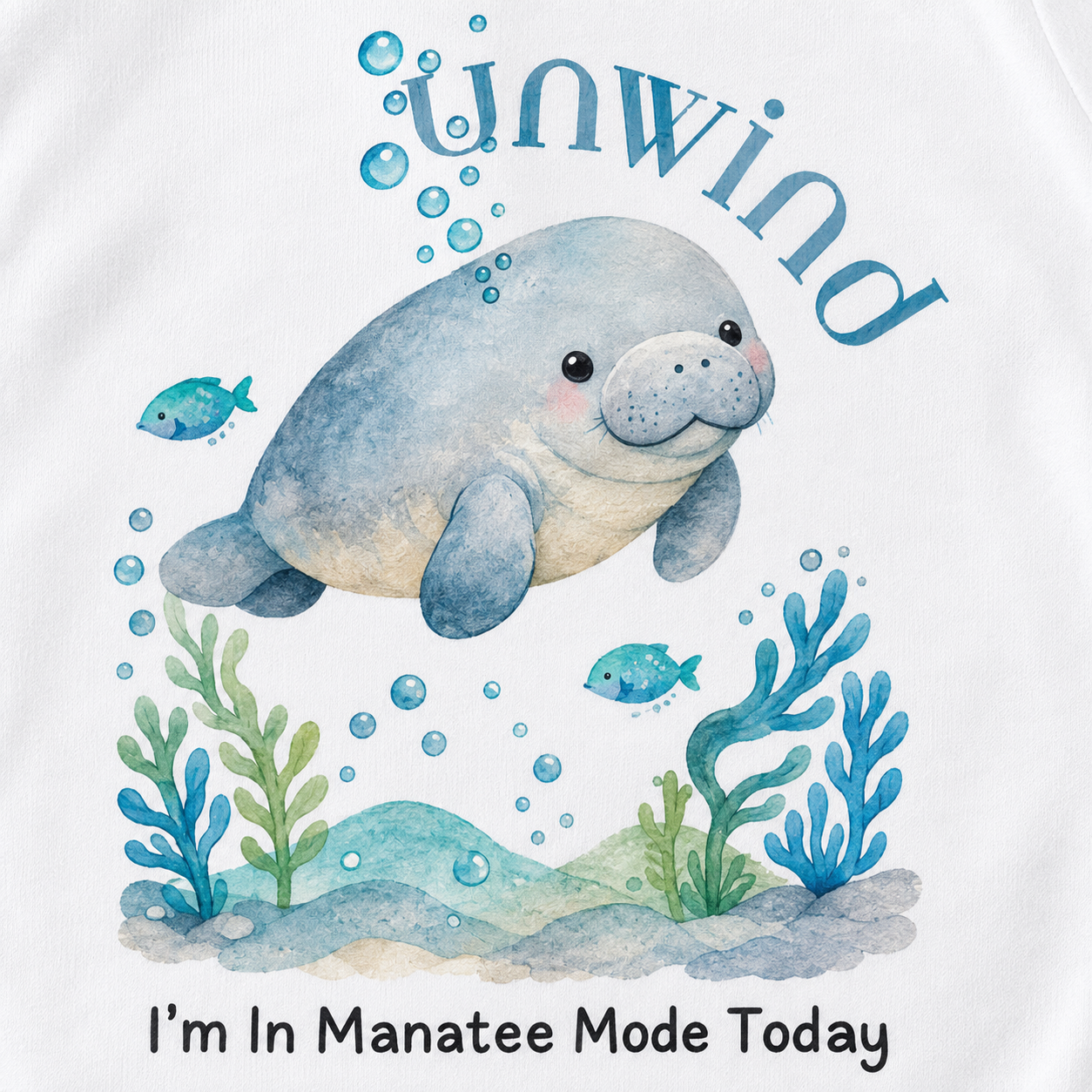 A white graphic t-shirt featuring a watercolor illustration of a smiling manatee swimming underwater with blue fish, bubbles, and seaweed. The text 'unwind' is written above the manatee, and 'I'm In Manatee Mode Today' is printed below.