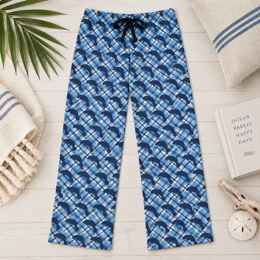 Blue plaid lounge pants with a navy dolphin print and a black drawstring, laid flat on a light wood surface with beach-themed props.