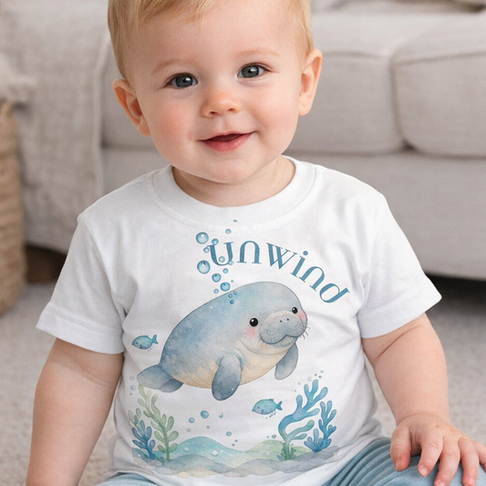 Baby wearing a white t-shirt with a seal design and text, sitting on a carpeted floor.
