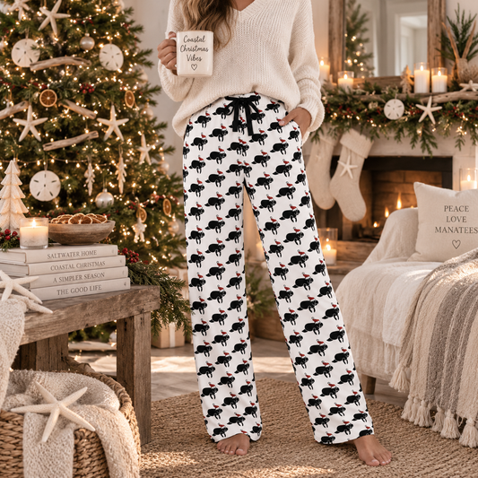 A person standing in a cozy holiday living room wearing white lounge pants with a black and red crab print, paired with a cream knit sweater and holding a mug that reads 'Limited Christmas Vibes'.
