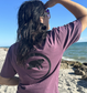 Lifestyle shot of a woman wearing Midnight Grape Manatee Wave T-Shirt from the back, showing relaxed fit and unique wave design.