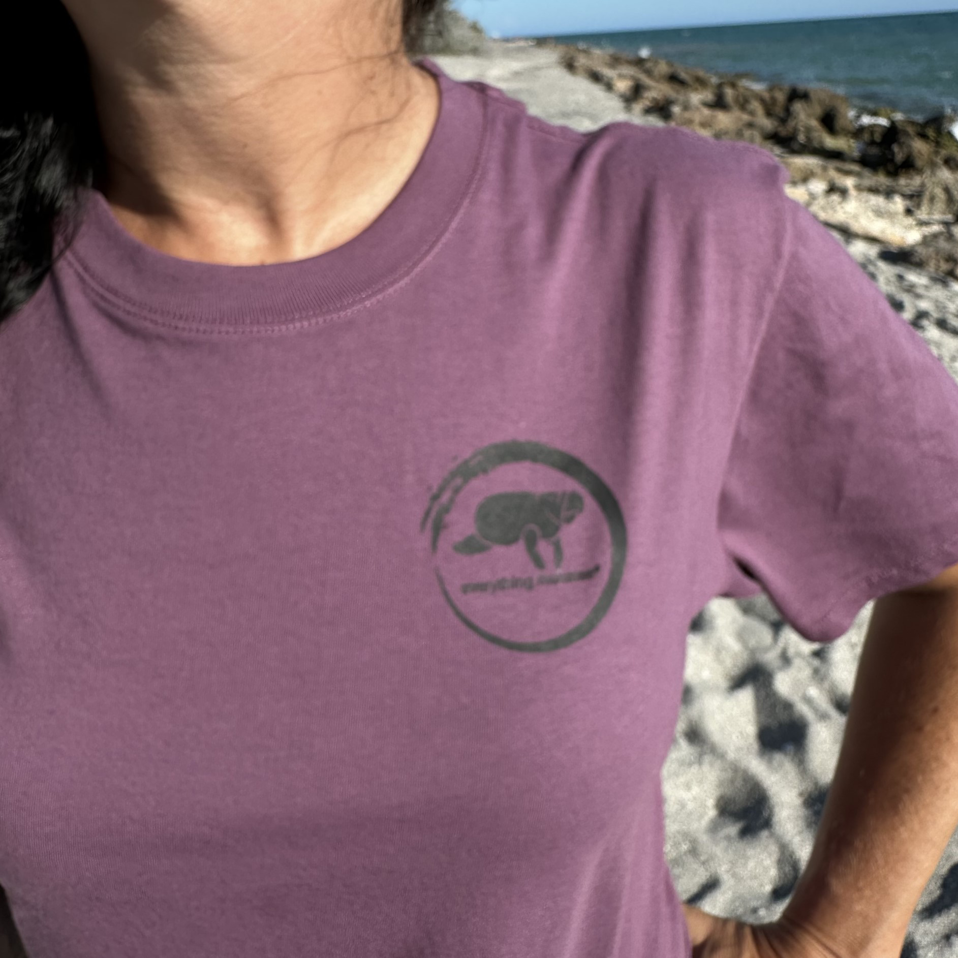 Lifestyle shot of a woman wearing Midnight Grape Manatee Wave T-Shirt from the front, featuring a playful manatee and lettering.