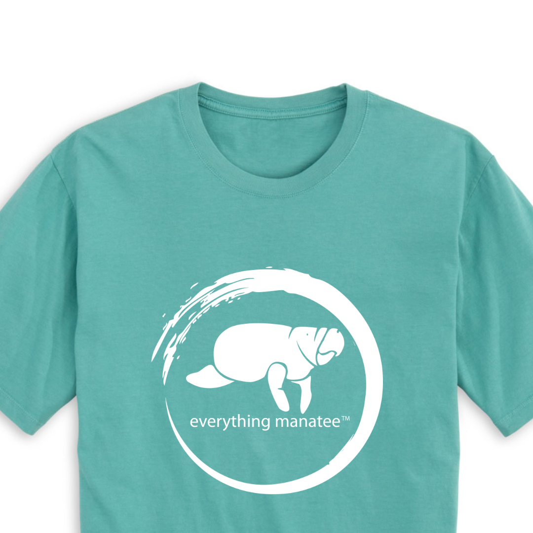 A close-up view of the front print design of the Seafoam Manatee Wave T-Shirt, featuring a striking illustration of a manatee swimming through waves and the word "Manatee" below it.