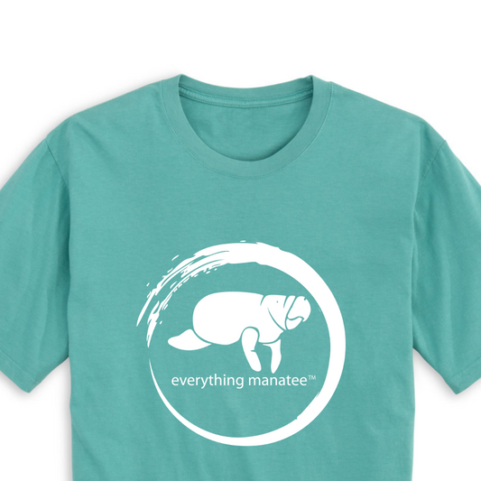 A close-up view of the front print design of the Seafoam Manatee Wave T-Shirt, featuring a striking illustration of a manatee swimming through waves and the word "Manatee" below it.
